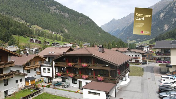 An alpine building with balconies and colorful flowers. In the background, green mountains and a tranquil landscape can be seen. - Hotel Garni Maria Theresia - Sölden