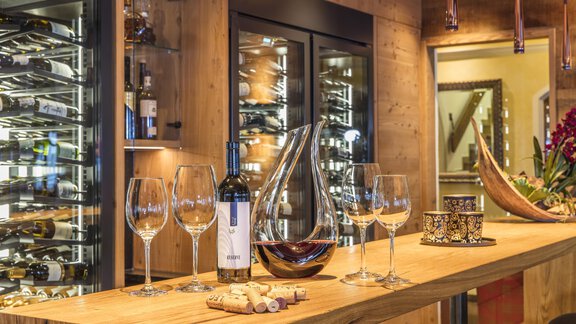 A stylish wine cellar with a wooden bar and elegant wine glasses. A bottle of wine and a decanter add an upscale touch to the ambiance. - Hotel Hubertus - Sölden