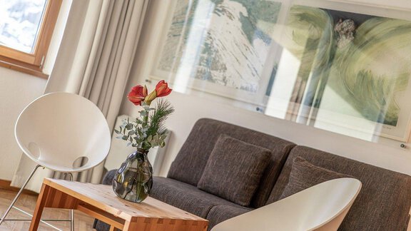 A modern living room with a gray sofa and two chairs. On a wooden table, there is a vase with flowers. - Hotel Liebe Sonne - Sölden