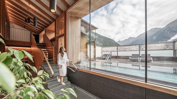 A modern spa with an indoor pool and a view of the mountains. A woman in a bathrobe enjoys the relaxing atmosphere. - Hotel Liebe Sonne - Sölden