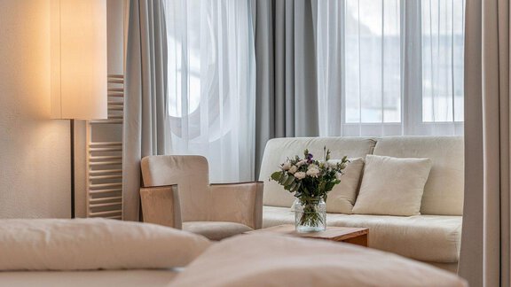A cozy room with a comfortable sofa and a chair.  
On the table, there is a vase of flowers, and the light is bright and inviting. - Hotel Liebe Sonne - Sölden
