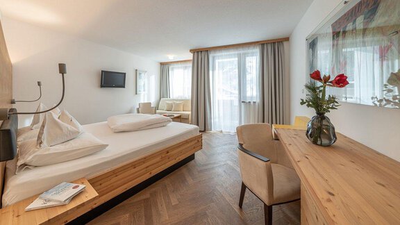 A modern hotel room with a large bed and wooden decor. The room has windows with a view outside and a wooden desk. - Hotel Liebe Sonne - Sölden