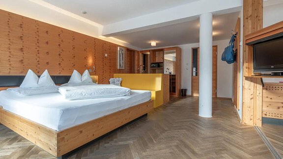 A modern hotel room with wooden walls and a large bed. The room is bright and welcoming, featuring a television and a small kitchenette. - Hotel Liebe Sonne - Sölden