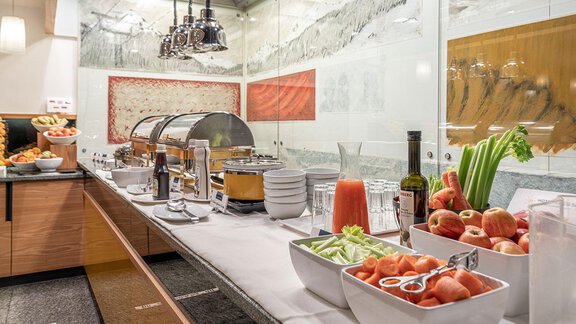 A buffet with various dishes and drinks in a modern environment. Fresh fruits and vegetables are arranged in bowls on a long table. - Hotel Liebe Sonne - Sölden