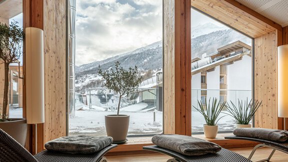 A bright room with large windows offering a view of snow-covered mountains. In the foreground are cozy lounges and plants. - Hotel Liebe Sonne - Sölden