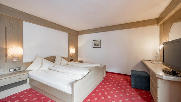 A bright hotel room with two single beds and a cozy carpet. Next to the bed is a television and a small table. - Hotel Sölderhof - Sölden