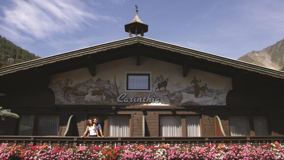 A traditional alpine house with an artistically painted facade. Blooming plants decorate the balcony and the surroundings. - Hotel Sportpension Carinthia - Sölden