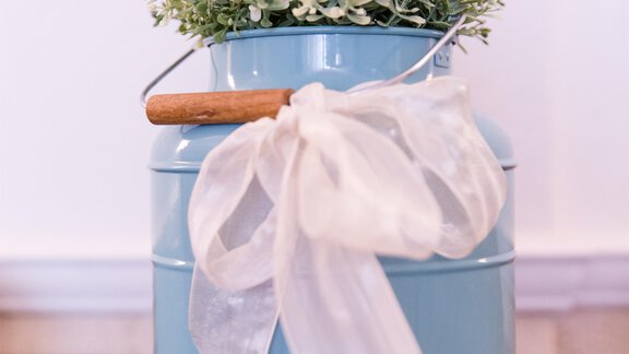A blue metal kettle with a wooden handle and a bow. Inside, there is a small plant with green leaves. - Hotel Sportpension Carinthia - Sölden