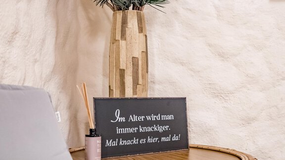 A table with a decorative vase and a sign with a humorous saying about age. Next to it is a scent diffuser and some sticks. - Hotel Sportpension Carinthia - Sölden