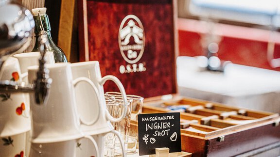 A stylish bar area with decorative cups and glasses. A table includes a wooden box with a sign for a ginger shot. - Hotel Sportpension Carinthia - Sölden