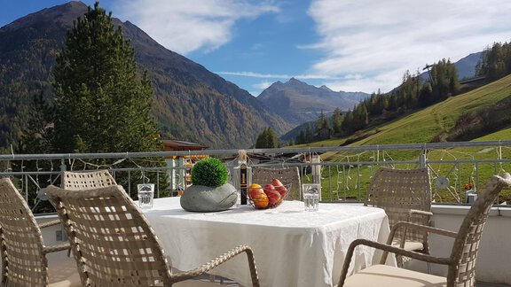 A beautiful view from a terrace of mountains and green meadows. The table is decorated with fruit and offers an inviting atmosphere. - Hotelappart Peter - Sölden