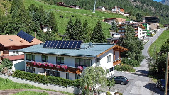 A modern house with solar panels and a flower balcony in a picturesque mountain landscape. In the background, green hills and other buildings can be seen. - La Luna - Sölden