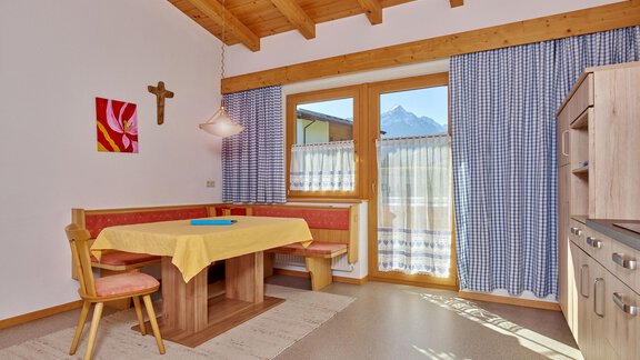 Eine helle Küche mit einem Holzdecke und einem großen Fenster. Der Tisch ist mit einer gelben Tischdecke gedeckt und es gibt bunte Vorhänge. - La Luna - Sölden