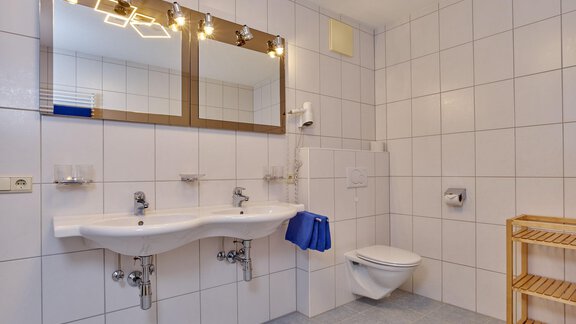 Ein modernes Badezimmer mit hellen Fliesen und zwei Waschbecken. Es gibt einen WC-Bereich und einen Holzregal für Handtücher. - La Luna - Sölden
