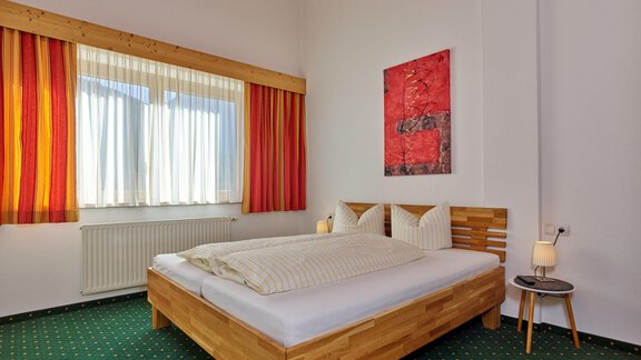 Ein gemütliches Schlafzimmer mit einem Holzbett und farbenfrohen Vorhängen. An der Wand hängt ein modernes Kunstwerk. - La Luna - Sölden