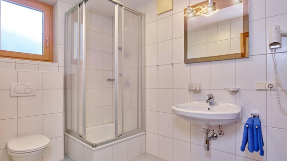 Ein modernes Badezimmer mit Dusche, Waschbecken und Toilette. Helle Fliesen und ein Fenster sorgen für ein angenehmes Ambiente. - La Luna - Sölden