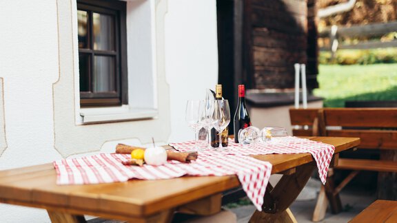 A tastefully set table outdoors with red and white tablecloths. On the table are wine glasses and bottles, surrounded by a cozy atmosphere. - Landhaus Peater's Hoamat - Sölden