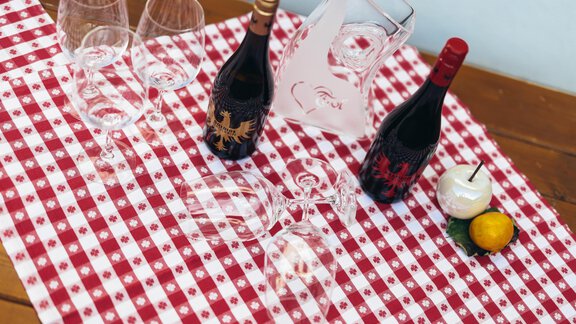 A table set with a red checkered cloth, two bottles of wine, and wine glasses. A water pitcher and a decoration made of fruit complete the picture. - Landhaus Peater's Hoamat - Sölden