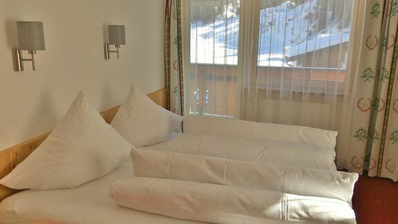 A cozy bedroom with a large double bed and white pillows. Large windows let in plenty of light and offer a view of the snowy landscape. - Landhaus Vinzenz - Sölden