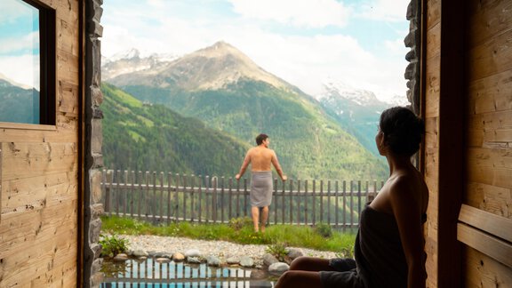 A relaxing wellness area with a sauna and a view of the mountains. Outside, a person can be seen by the pool enjoying the view. - LENI MOUNTAIN CHALET - Sölden
