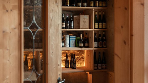 A cozy room with wooden walls and shelves full of bottles. The lighting creates an inviting atmosphere. - LENI MOUNTAIN CHALET - Sölden