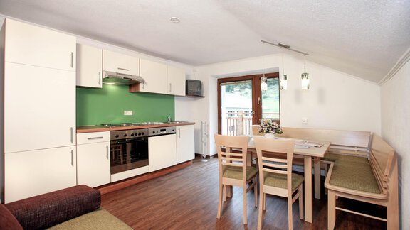 A modern kitchen with a wooden floor and a dining area. The color scheme is bright with a green accent. - Lutonia Appartements Sölden - Sölden
