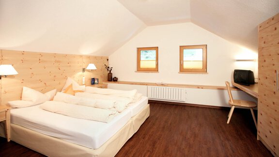 A cozy bedroom with a double bed and wood-paneled walls. There are two windows and simple furniture for a clear, calm style. - Lutonia Appartements Sölden - Sölden