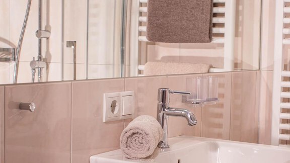 A modern bathroom with an elegant sink and towels. In the background, large tiles and a shower are visible. - Lutonia Appartements Sölden - Sölden