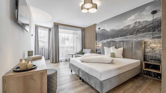 A modern bedroom with a large bed and stylish decor. The wall behind the bed features a mountain panorama, and large windows provide plenty of daylight. - Marco's Mountain Home - Sölden