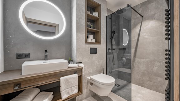A modern bathroom with a glass shower and stylish fixtures. The walls are neutrally tiled, and there is an elegant sink as well as towels on a wooden shelf. - Marco's Mountain Home - Sölden