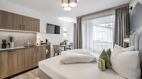 A modern hotel room with a comfortable bed and a kitchenette. Large windows provide plenty of daylight and a cozy atmosphere. - Marco's Mountain Home - Sölden