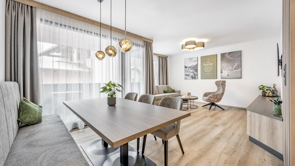 A modern and bright living room with a large dining table group and comfortable seating. The windows are dressed with elegant curtains that bring a lot of daylight in. - Marco's Mountain Home - Sölden