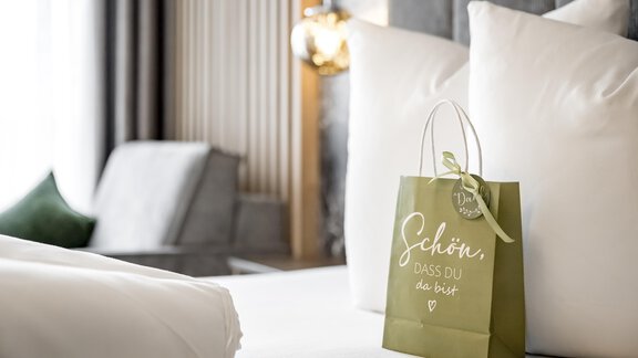A stylish hotel room with a large bed and decorative pillows. A green gift bag with the inscription "Nice to have you here" is on the bedspread. - Marco's Mountain Home - Sölden