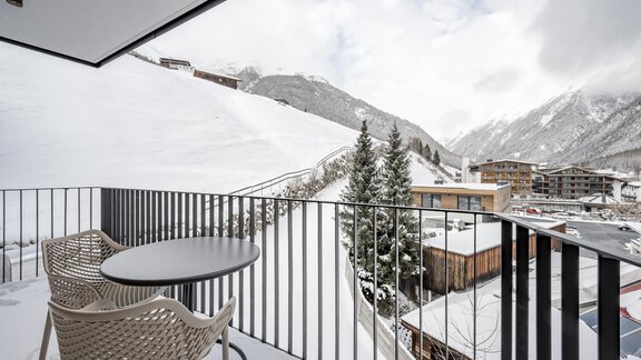 A balcony with a small table and chairs, from which one can see the snowy landscape and the mountains. The surroundings feel calm and wintry. - Marco's Mountain Home - Sölden