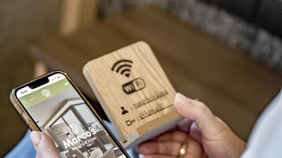 A person is holding a smartphone and looking at an app. Next to them is a wooden Wi-Fi hotspot. - Marco's Mountain Home - Sölden