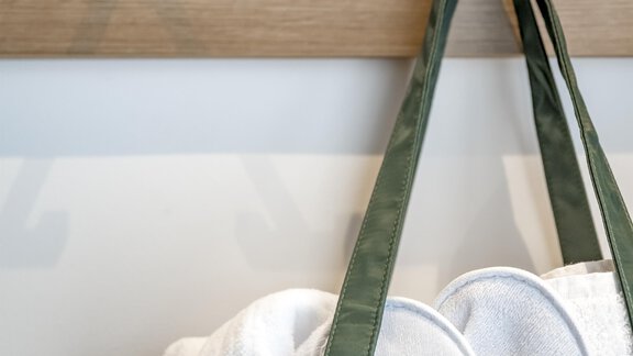 A green bag with white towels hangs on a wooden coat rack. In the background, two black hooks are visible. - Marco's Mountain Home - Sölden