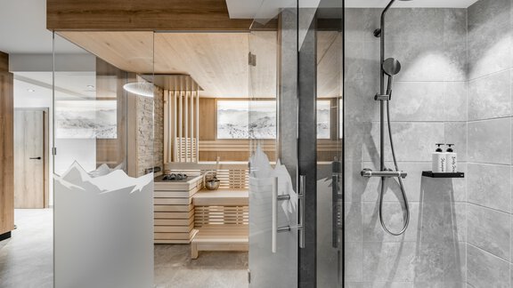 A modern bathroom with a clear shower enclosure and wooden details. In the background, there is a sauna with a minimally designed layout. - Marco's Mountain Home - Sölden