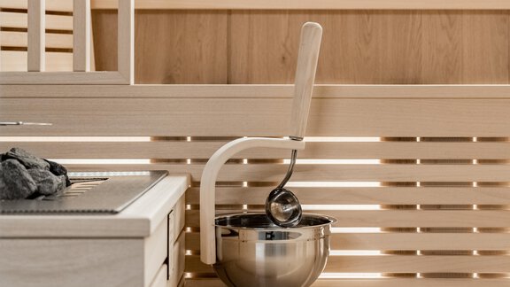 A modern sauna with bright wood interiors. A ladle hangs in a stainless steel bowl, ready for use. - Marco's Mountain Home - Sölden