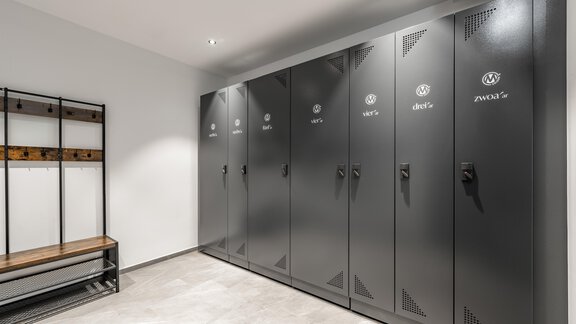A modern changing room with gray lockers on the wall. On the right, there is a wooden bench for changing. - Marco's Mountain Home - Sölden