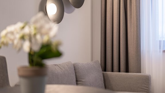 A modern living room with a gray sofa and decorative wall lights. A small potted plant sits on the table. - Pension Miramonte - Sölden