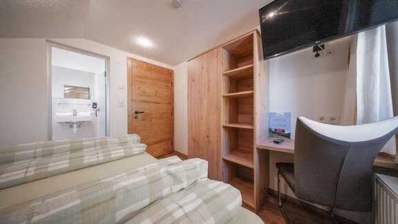 A cozy room with wooden details and modern furniture. There is a comfortable bed, a desk, and a television. - Pension Pitze - Sölden