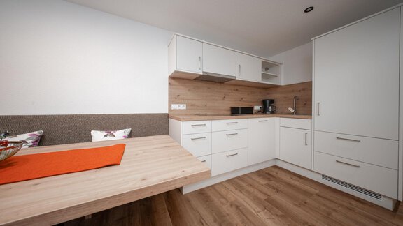 A modern kitchen with white cabinets and a wood countertop. The dining area is designed simply and warmly. - Pension Pitze - Sölden