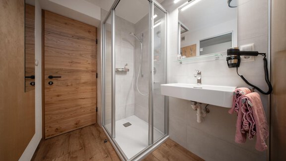 A modern bathroom with a glass shower and an elegant sink. The floor is made of wood, and there is a wooden closure. - Pension Pitze - Sölden