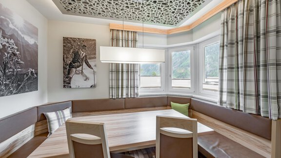 A modern dining room with a large wooden table and elegant chairs. The walls are adorned with windows and decorative curtains as well as artworks. - Residenz Allegra - Sölden