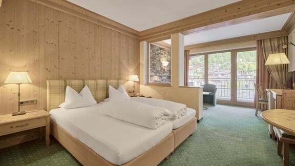 A cozy hotel room with two single beds and wooden paneling. Generous windows offer a view of the surroundings. - Riders In - Sölden
