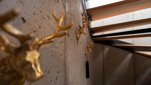 An elegant staircase with modern golden wall decorations. The background is made of concrete, creating a stylish contrast. - Selda Chalet - Sölden