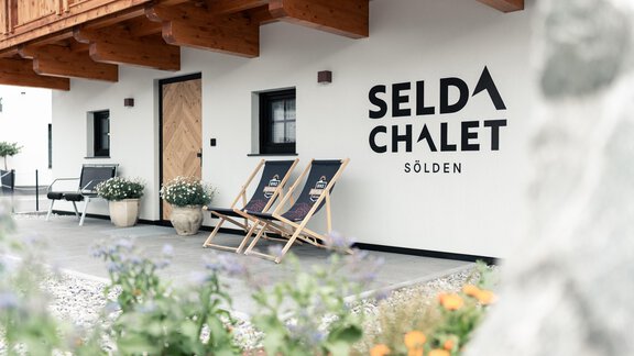 A modern chalet with the inscription "SELDA CHALET" in Sölden. There are comfortable lounge chairs and flowers in front of the entrance door. - Selda Chalet - Sölden