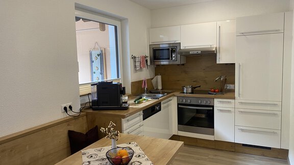 A modern kitchen with bright furniture and a wooden countertop. On the table, there is a fruit bowl and in the background, there is a microwave. - Sportpension Rubin - Sölden