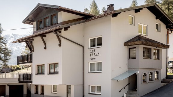 A modern building with several windows and an inviting entrance. The house has an alpine style and is surrounded by trees. - THE BLACK by Regina - Sölden