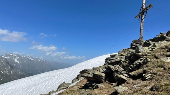 A mountain peak with a wooden cross and snow-covered slopes. The sky is blue with some clouds. - Top Apart Daniela - Sölden